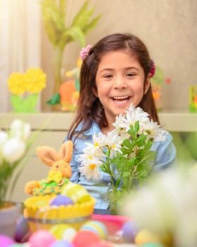Portrait of cheerful smiling little girl sitting in the child’s room with beautiful daisy flower bouquet, celebrating Easter holiday, happy spring season