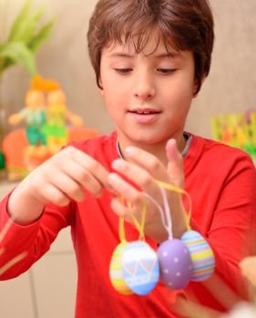 Portrait of cute boy play with beautiful colorful decorated eggs at home, with pleasure anticipate happy Easter holiday

