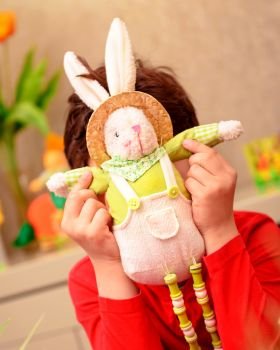 Joyful boy playing with soft bunny toy at home, traditional Easter symbol, happy preparation to religious spring holiday