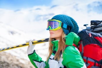 Portrait of healthy woman wearing sportive mask and holding ski in hands, spending winter holidays in snowy mountains