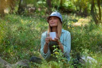 Beautiful Woman Drinking Tea and Chilling in the Forest. Vacation Time. Peaceful Time. Blond Female is Having a Break. Relax the Mind.. Woman in the Forest Drinking Tea