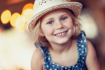 Portrait of nice little smiling girl wearing straw sun hat, enjoying sunny summer holidays, happy healthy childhood