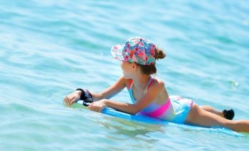 Happy cheerful little girl swimming in the sea on a bodyboard, summertime activities, enjoying summer holidays on the beach resort