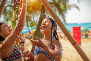 Two little girls playing with outdoor shower, best friends having fun in hot sunny day on the beach, enjoying active summer holidays
