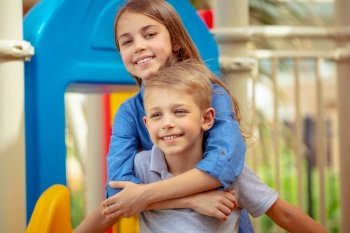 Portrait of a cute siblings having fun together on playground, brother and sister with pleasure spending summer holidays outdoors on back yard