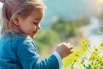 Profile portrait of a happy cute little baby having fun outdoors, enjoying small yellow wildflowers, beauty of spring nature