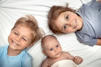 Portrait of a Three Cute Little Kids Lying Down on the Bed at Home. Adorable Siblings Having Fun Together. Happy Family Life
