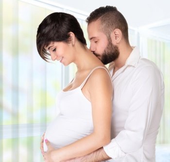 Young couple awaiting baby, handsome man hugging his nice pregnant wife and kiss her neck, happy and healthy pregnancy
