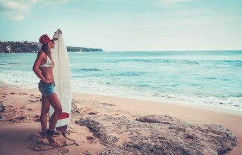 Beautiful surfer girl standing on the beach with surfboard, attractive sportive female with perfect body, enjoying summer holidays and watersport