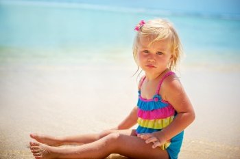 Portrait of a adorable pretty child on the beach, cute little blond girl wearing nice colorful swimsuit sitting on the sandy coast