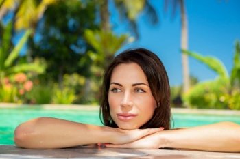 Portrait of a beautiful calm woman in a swimming pool, relaxing in a cold refreshing water on hot summer day, spending holidays on tropical beach resort, day spa