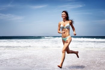 Beautiful sportive woman running on a beach, doing sport exercise on seashore in hot summer day, enjoying freedom, happy healthy lifestyle
