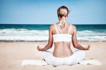 Woman meditating on the beach, rear view of a slim healthy girl sitting in lotus pose and enjoying beautiful view of a sea, mindfulness