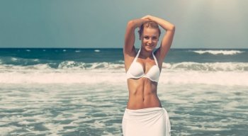 Beautiful woman having fun on the beach, attractive model posing on the seashore, enjoying summer vacation