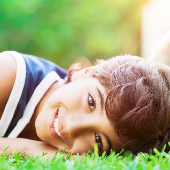Closeup portrait of a happy smiling boy lying down on the fresh green grass in bright sunny day, enjoying summer holidays in countryside