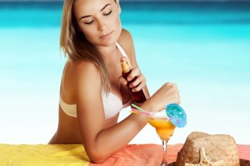 Beautiful girl sunbathing on the beach, uses a sunscreen spray for a safe tan, fun summer vacation near the sea, skin care concept
