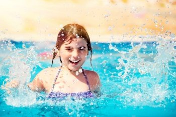 Portrait of a smiling little girl playing in the pool, splashing water, happy summertime activity, enjoying summer holidays on the beach resort