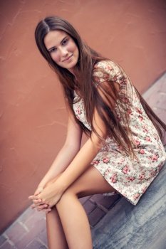 Portrait of a pretty brunette girl sitting on the street, nice attractive model with natural long hair, authentic people