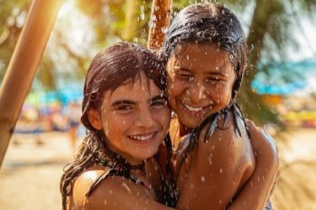 Portrait of a two happy little girls standing together under the shower on the beach, best friends with pleasure spend summer holidays near the sea