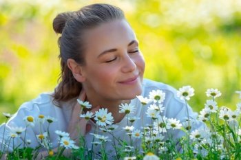 Portrait of a happy female having fun on the fresh daisy flowers field, enjoying warm sunny spring day and aromaof flowers