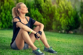 Beautiful athletic woman resting on green grass lawn after a good workout, tanning and enjoying music, harmony and soul balance concept
