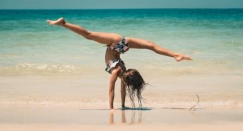 Little Sportive Girl with Pleasure Practicing Acrobatic Tricks on the Beach. Doing Sport Outdoors. Healthy Lifestyle. Happy Summer Vacation.. Little Girl Athlete on the Beach