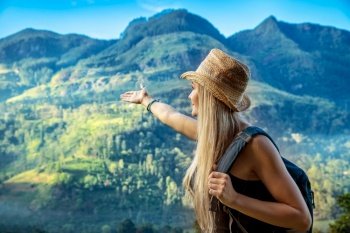 Happy young traveler girl showing by hand on a great mountain covered with dense forest, enjoying amazing tropical nature of Sri Lanka