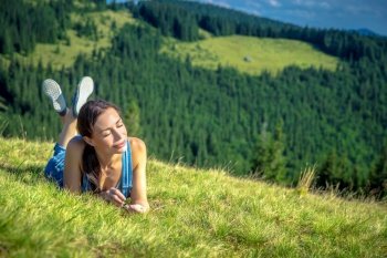 Happy girl chilling in Carpathian mountains, lying down on fresh green grass, enjoying sun rays and clear air, peaceful summer vacation, west Ukraine
