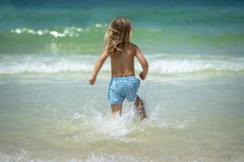Back Side of a Little Boy Running in the Water Making Splashes. Happy Child Enjoying Active Summer Holidays on the Beach Resort.. Happy Little Boy on the Beach