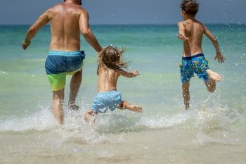 Father with Two Sons Running Away in the Sea. Playing Games and Making a Lot of Water Splashes. Happy Family Having Fun on the Beach.. Happy Family on the Beach