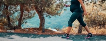 Sportive Pregnant Woman Jogging in the Mountainous Forest in Sunny Day. Enjoying the Walk Among Fresh Pine Trees. Body Part. Healthy Pregnancy.. Pregnant Woman Jogging in the Park