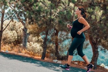 Happy Pregnant Woman on Workout in the Park on Sunny Day. Enjoying Sportive Walk Among Beautiful Fresh Trees. Active Healthy Pregnancy.. Pregnant Woman Running