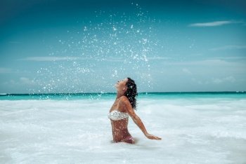 Beautiful Happy Girl Splashing Sea Water and Enjoying Bright Sun Light. Tanning on the Beach. Having Fun in Outdoor Resort. Happy Summer Vacation.. Cheerful Female on the Beach