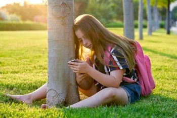 Blond student kid girl with smartphone in a park back to school sit on grass
