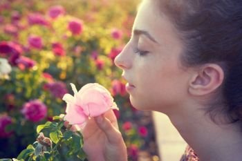 Profile portrait girl smelling a rose flower in a park