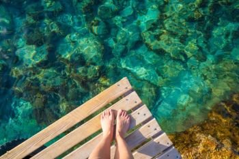 Ibiza girl legs at Portinatx beach pier clear water in Balearic Islands