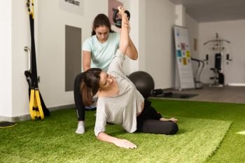 Physical therapist assisting young caucasian woman with exercise with dumbbell during rehabilitation in the gym at hospital. Female physiotherapist training a patient in physiotherapy center.