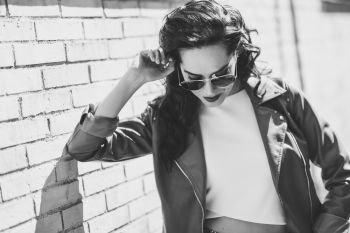 Young brunette woman with aviator sunglasses. Girl, model of fashion, wearing modern jacket, standing in urban background.