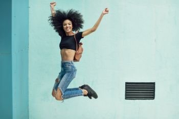 Young mixed woman with afro hair jumping outdoors. Female wearing casual clothes in urban background. Lifestyle concept