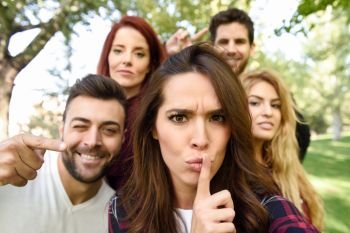 Group of friends taking selfie in urban background. Five young people wearing casual clothes. Woman doing shh gesture