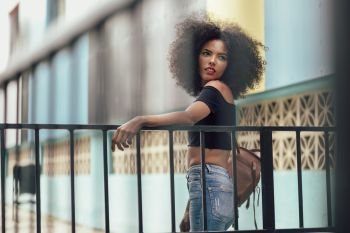 Young mixed woman with afro hair standing on the street. Female wearing casual clothes in urban background. Lifestyle concept