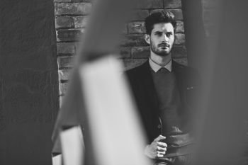 Attractive man in the street wearing british elegant suit. Young bearded businessman with modern hairstyle in urban background. Black and white photograph.