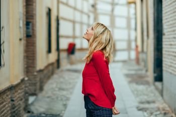 Happy young blond woman walking down the street. Smiling blonde girl with red shirt standing outdoors.