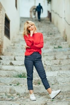 Happy young blond woman standing on beautiful steps in the street. Smiling blonde girl with red shirt standing outdoors.