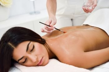 Arab woman receiving back massage treatment with oil brush in spa wellness center. Beauty and Aesthetic concepts.
