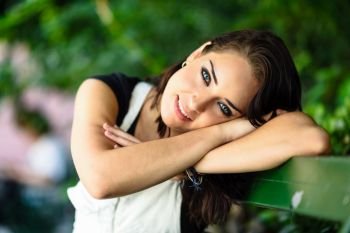 Happy young woman with blue eyes looking at camera sitting on urban bench. Smiling beautiful girl with sweet look.
