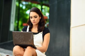 Beautiful young woman using laptop computer sitting on urban steps. Businesswoman wearing casual clothes working outdoors. Lifestyle concept.