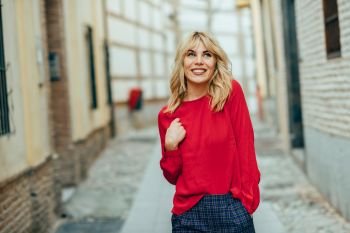 Happy young blond woman walking down the street. Smiling blonde girl with red shirt standing outdoors.