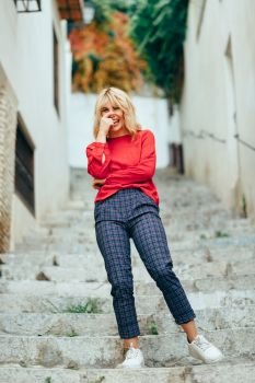 Happy young blond woman laughing on beautiful steps in the street. Smiling blonde girl with red shirt standing outdoors.. Happy young blond woman laughing on beautiful steps in the street.