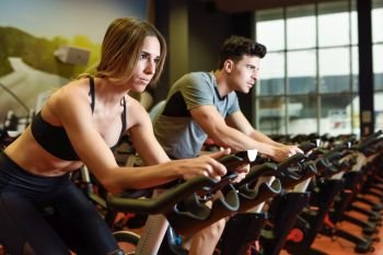Young man and woman biking in the gym, exercising legs doing cardio workout cycling bikes. Two people in a cyclo indoor class wearing sportswear.. Couple in a cyclo indoor class wearing sportswear.